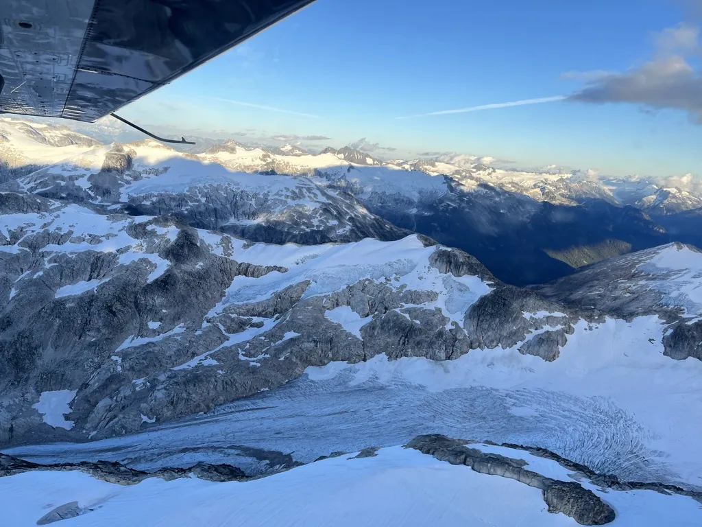 真夏のカナダの山岳地帯。小型機の翼の下に雪と氷河が広がる